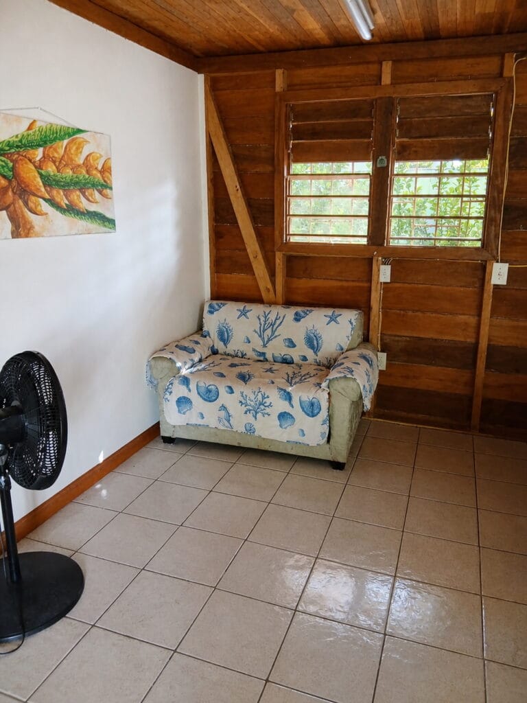 Sofa and standing fan in the wooden seating area of Cabana Cruz in Placencia, Belize
