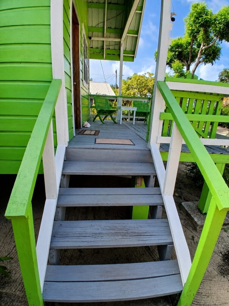 Green wooden entrance steps and furnished veranda at Cabana Menoma in Placencia, Belize